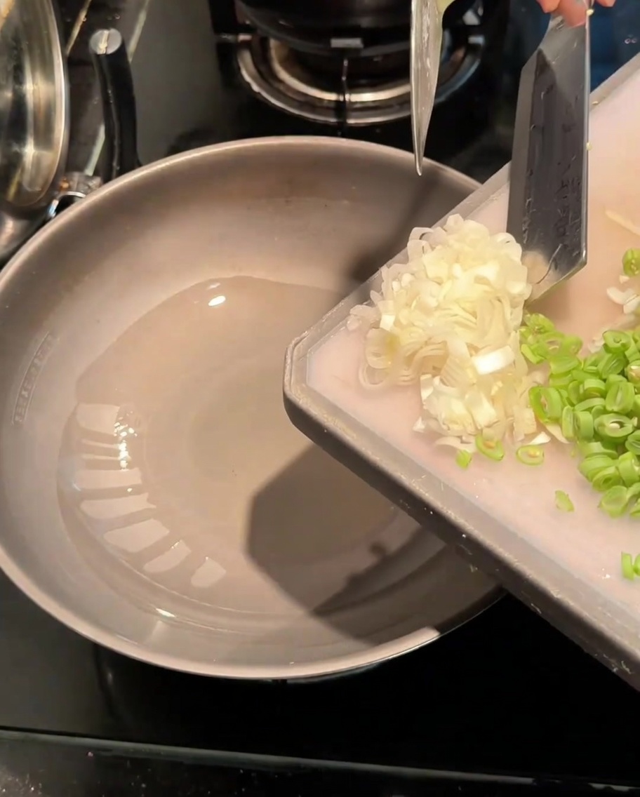Oignons verts hachés et haricots verts tranchés sautant dans un wok chaud avec de lhuile.