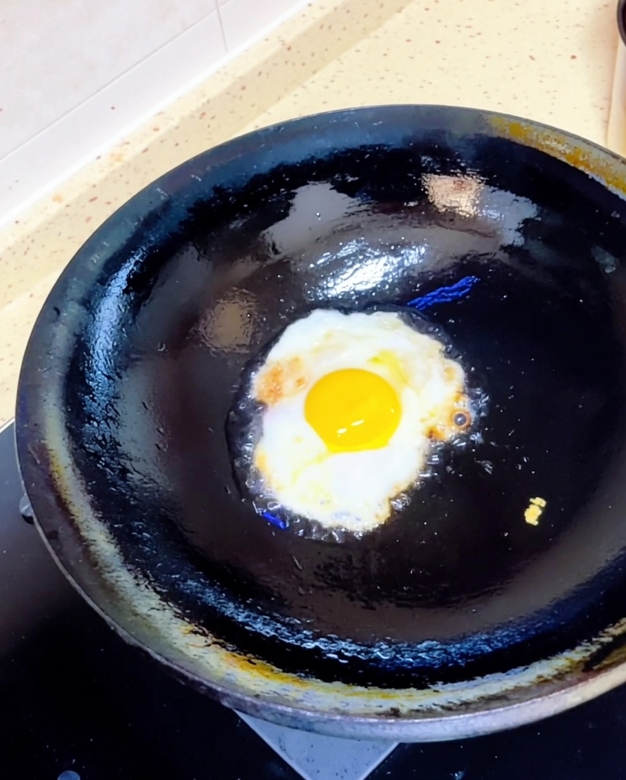Un œuf au plat grésillant dans un wok noir avec un peu dhuile chaude.
