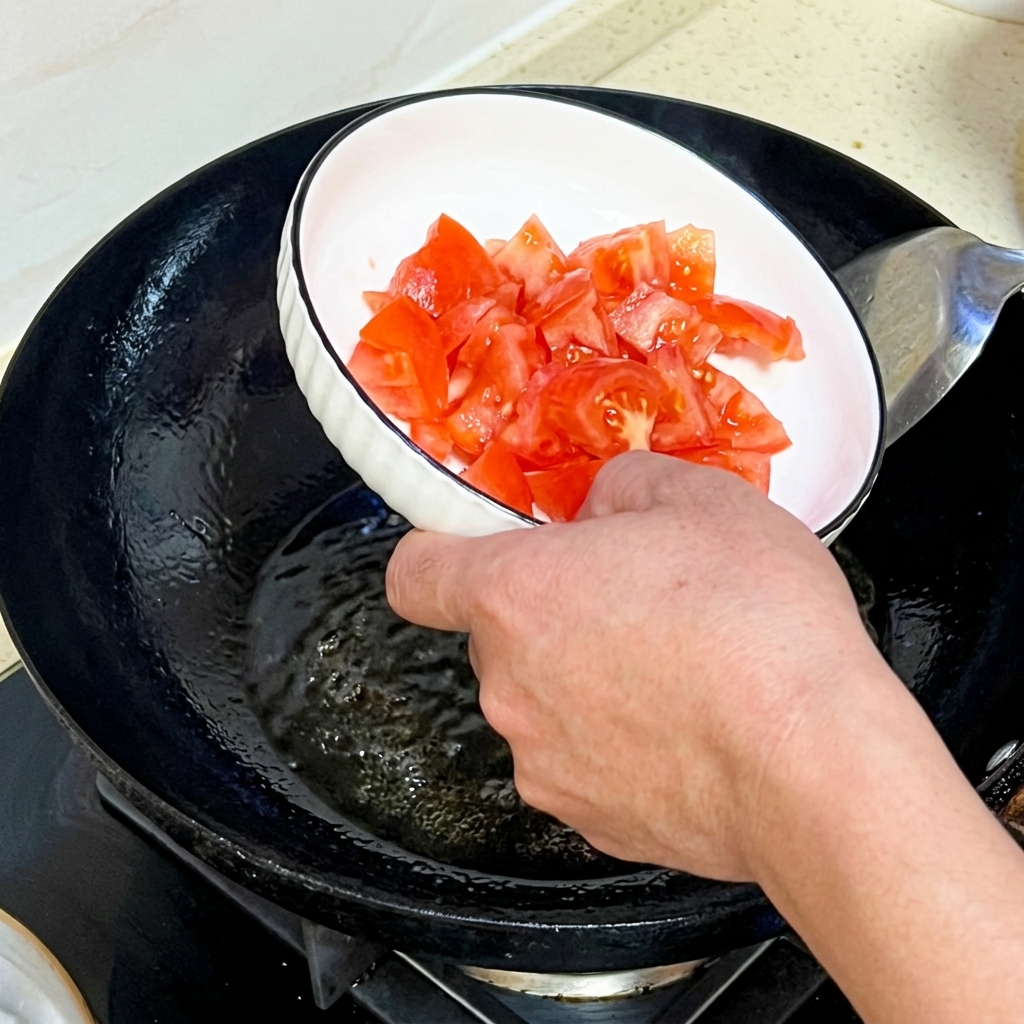 Une main versant des tomates fraîches hachées dans un wok.