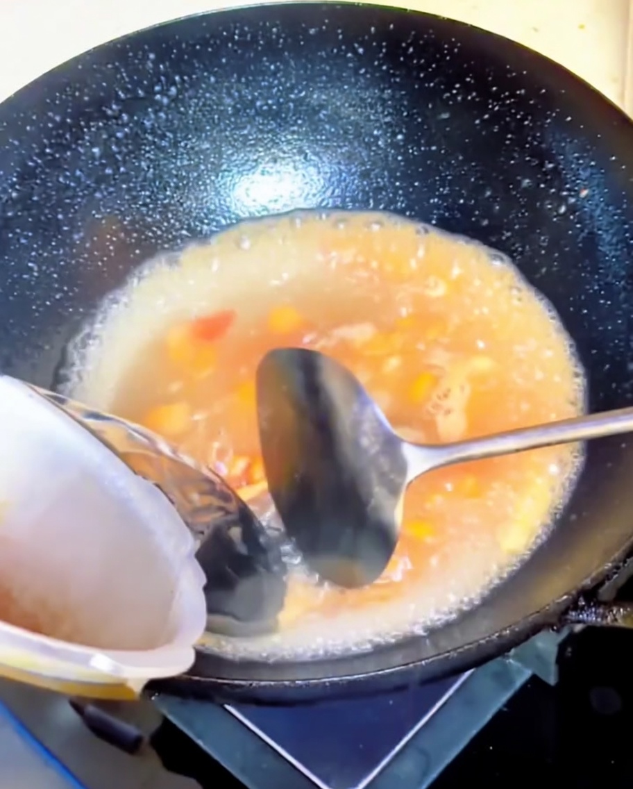 De leau versée dans un wok contenant une préparation de tomates mijotées.