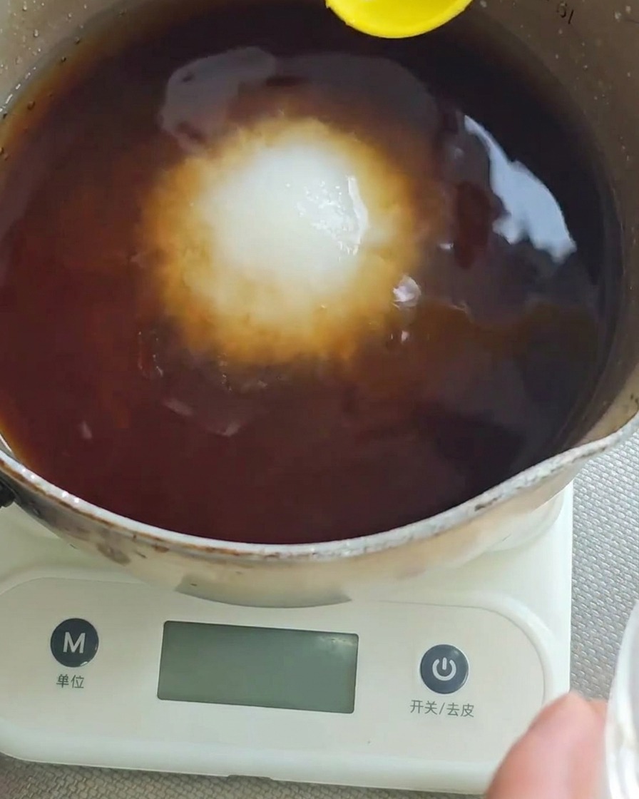 Une cuillère jaune ajoutant du sel blanc dans le mélange liquide foncé dans une casserole.