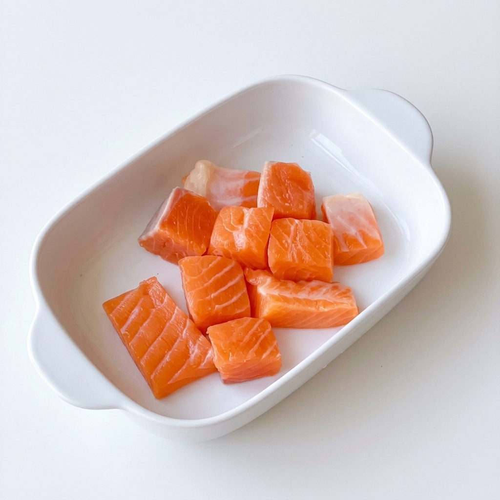 Cubes de saumon dans un bol en céramique, assaisonnés avec de lhuile dolive, du sel et du poivre.