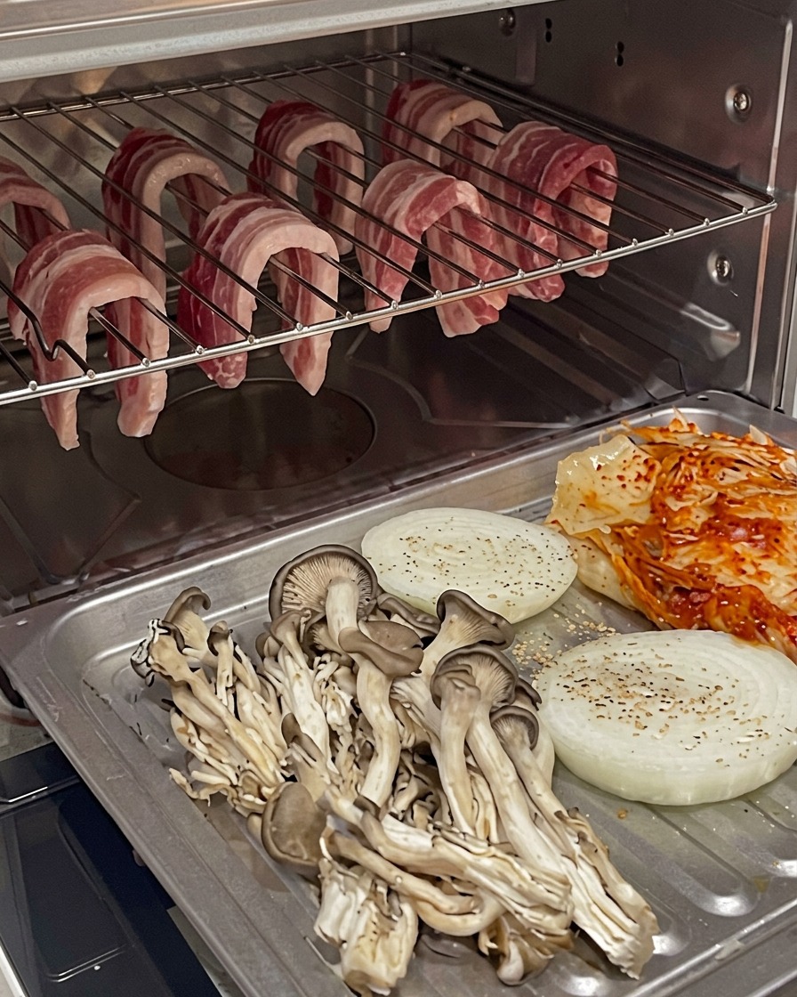 Plateau de cuisson avec légumes et kimchi positionné sous la poitrine de porc suspendue dans le four.