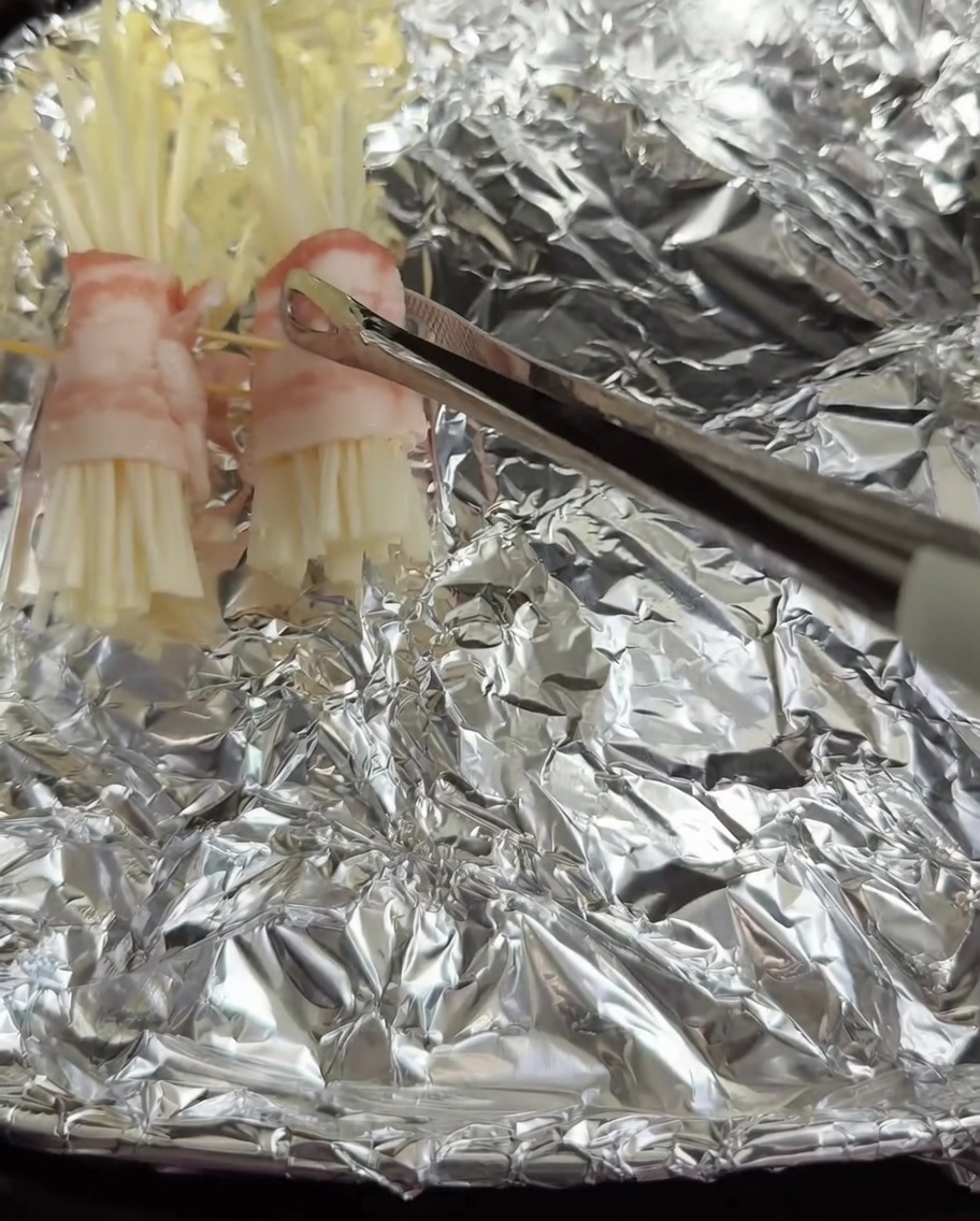 Roulés de porc aux enoki assemblés, placés dans un panier de friteuse à air recouvert de papier aluminium.