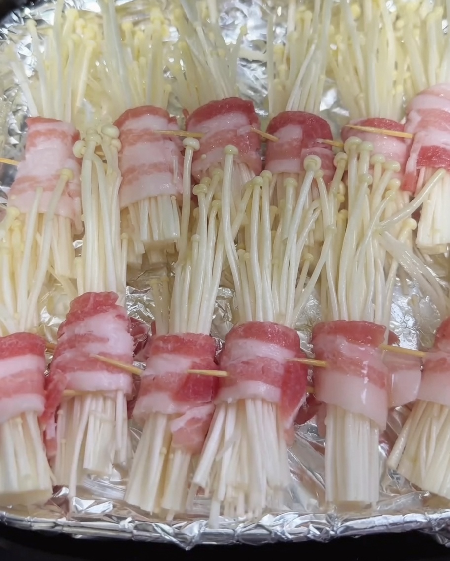 Spray appliquant une fine brume dhuile sur les roulés de porc aux champignons crus dans le panier de la friteuse.