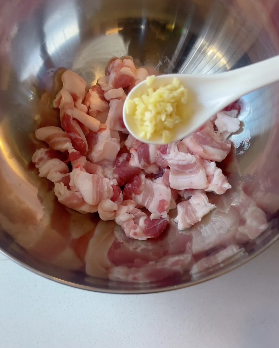 Tranches de poitrine de porc crue dans un bol en métal, avec de lail haché ajouté à la cuillère.