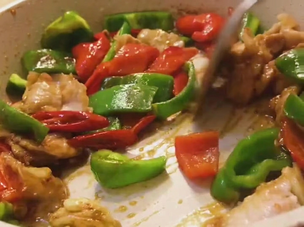 Un mélange de porc, de poivrons verts et de poivrons rouges remué dans une poêle avec une spatule en bois.
