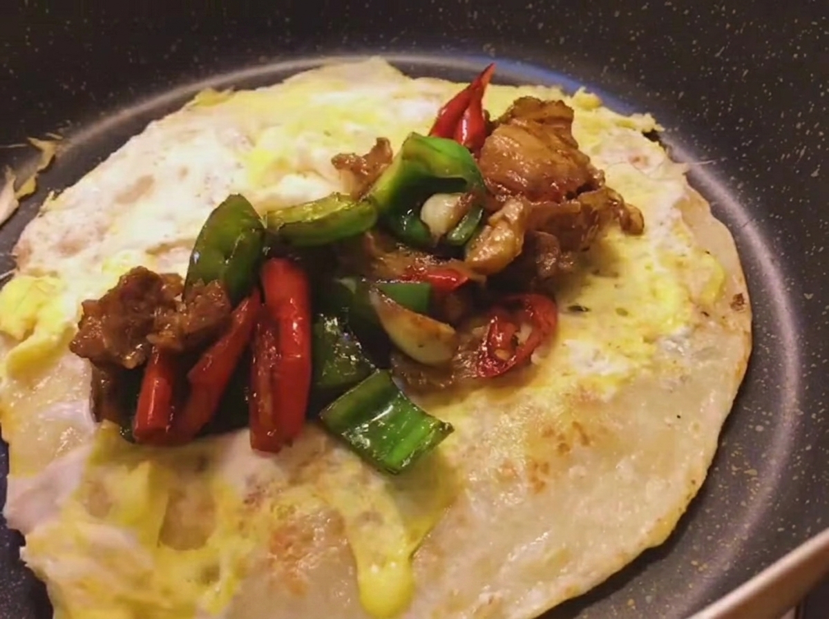 Garniture de porc et poivrons sautés épicés placée sur une crêpe à loignon dorée avec un œuf cuit sur le dessus.