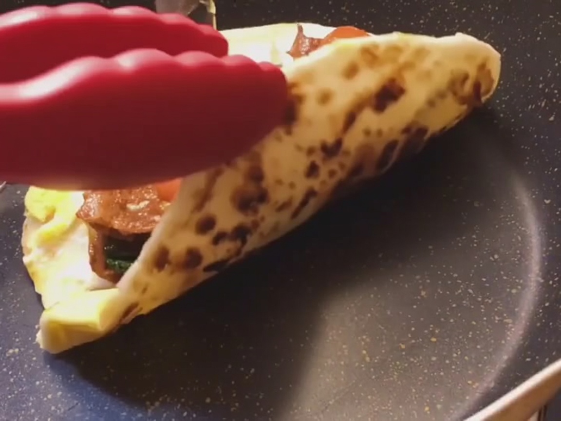 Un wrap de crêpe à loignon fraîchement préparé en train dêtre roulé fermement sur une surface plane.