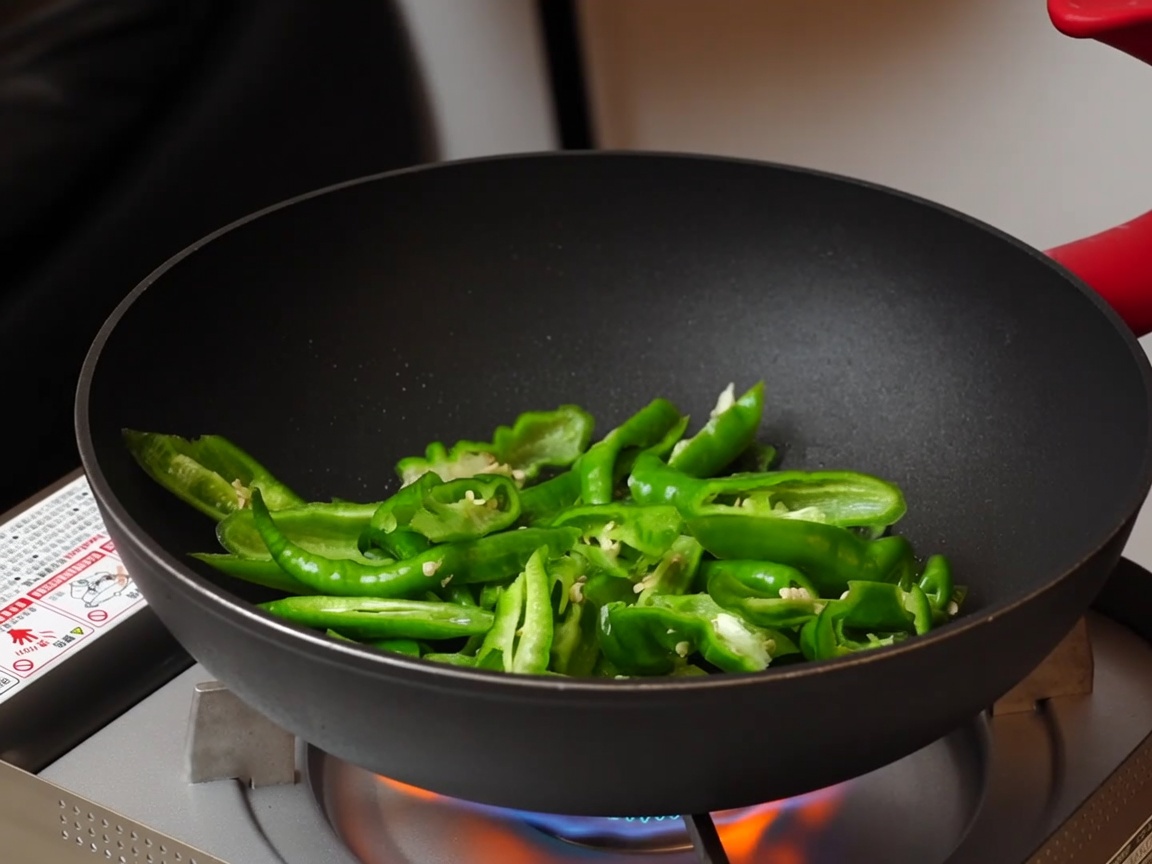 Piments en train de sauter dans une poêle antiadhésive sur un réchaud.