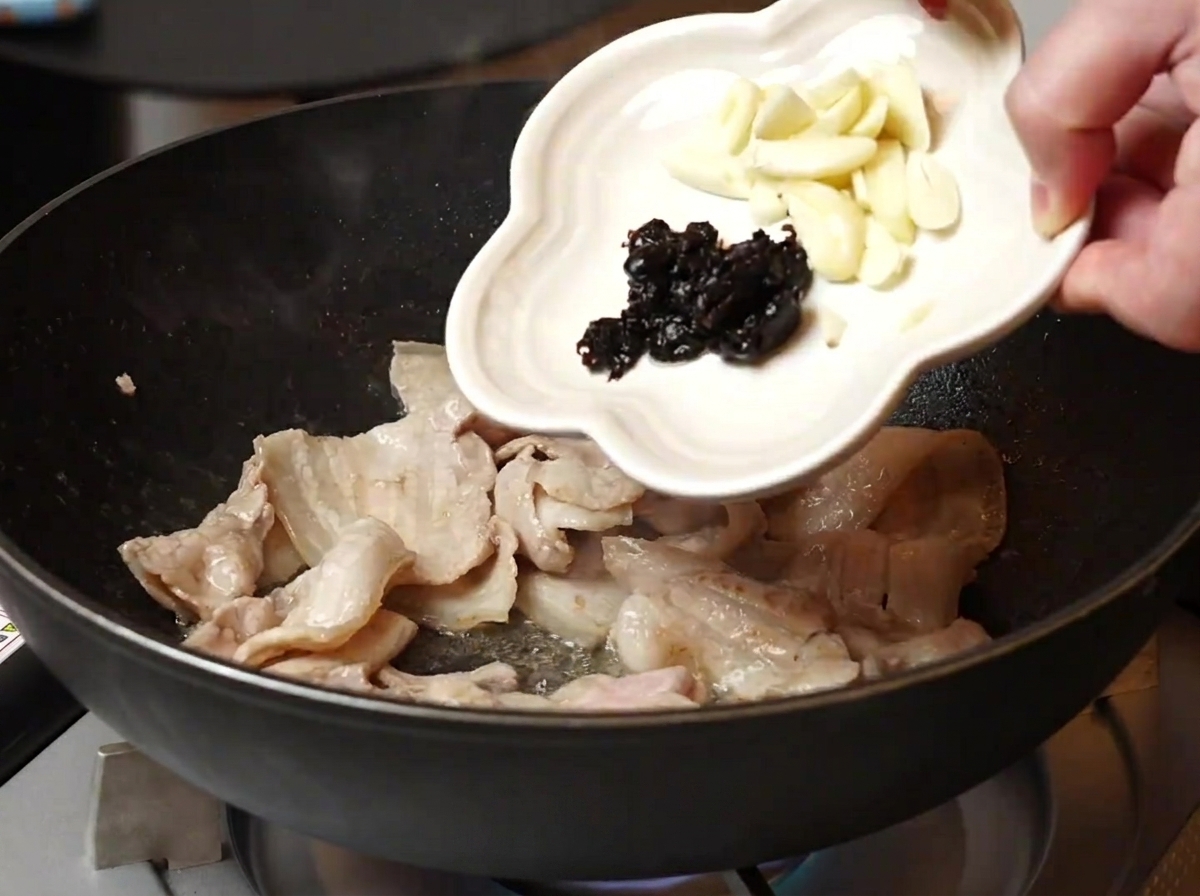 Ail et haricots noirs ajoutés dans la poêle contenant le porc doré.