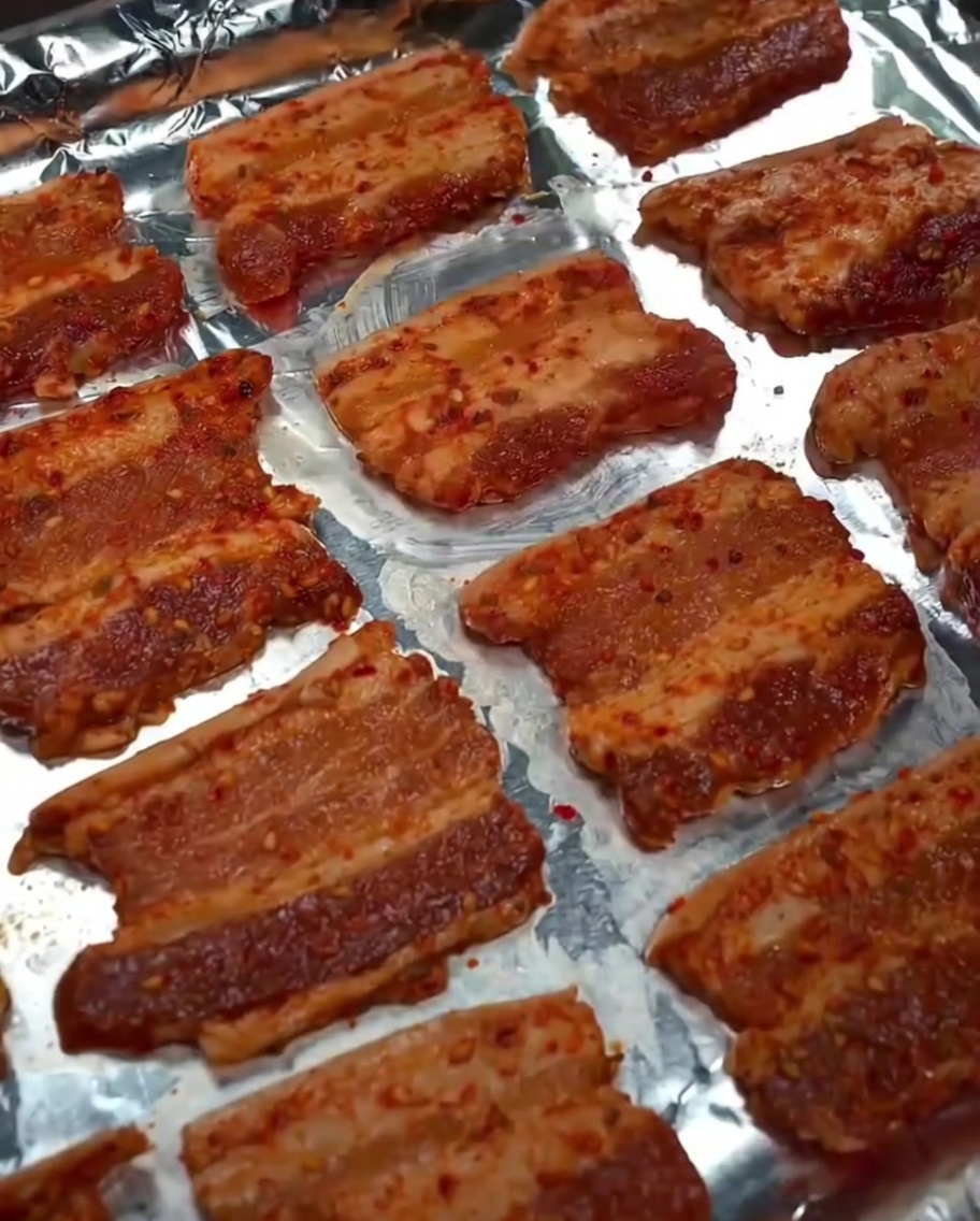 Huile de cuisson vaporisée sur les tranches de poitrine de porc sur la plaque.