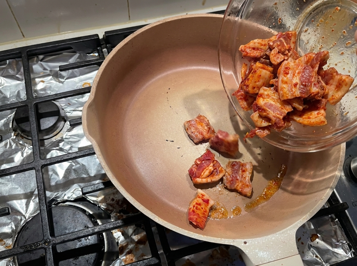 Tranches de poitrine de porc marinées glissant dun bol en verre dans une poêle chaude vide pour faire fondre le gras.
