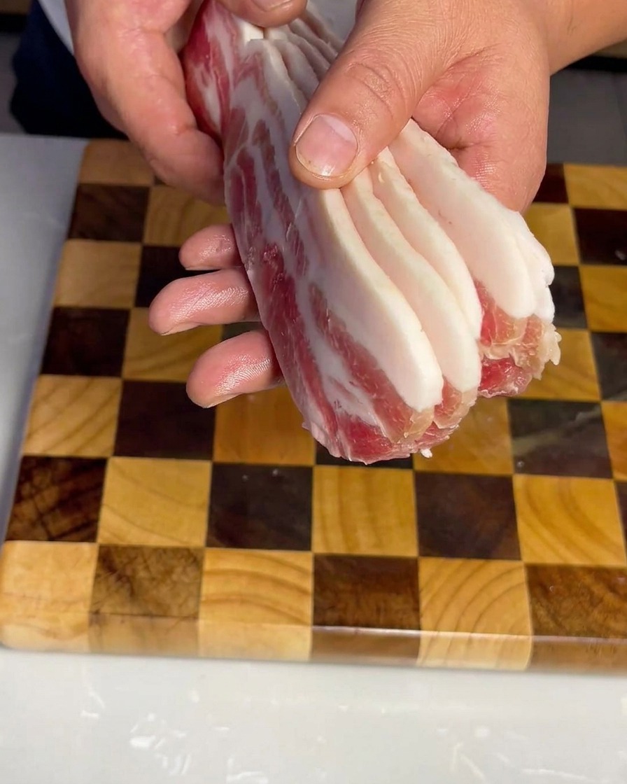Lanières uniformes de poitrine de porc crue soigneusement disposées sur une planche à découper en bois.