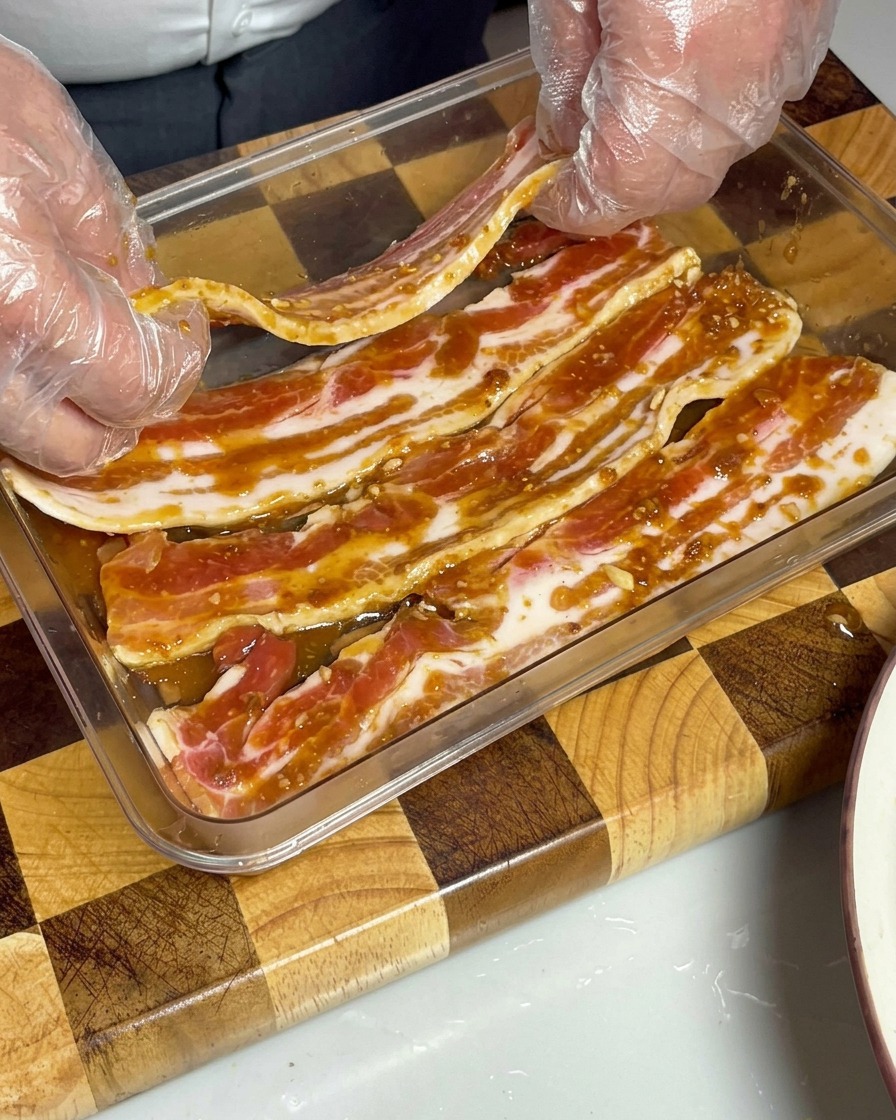 Lanières de poitrine de porc marinées soigneusement disposées dans un récipient transparent, entièrement recouvertes de la sauce miso brune.