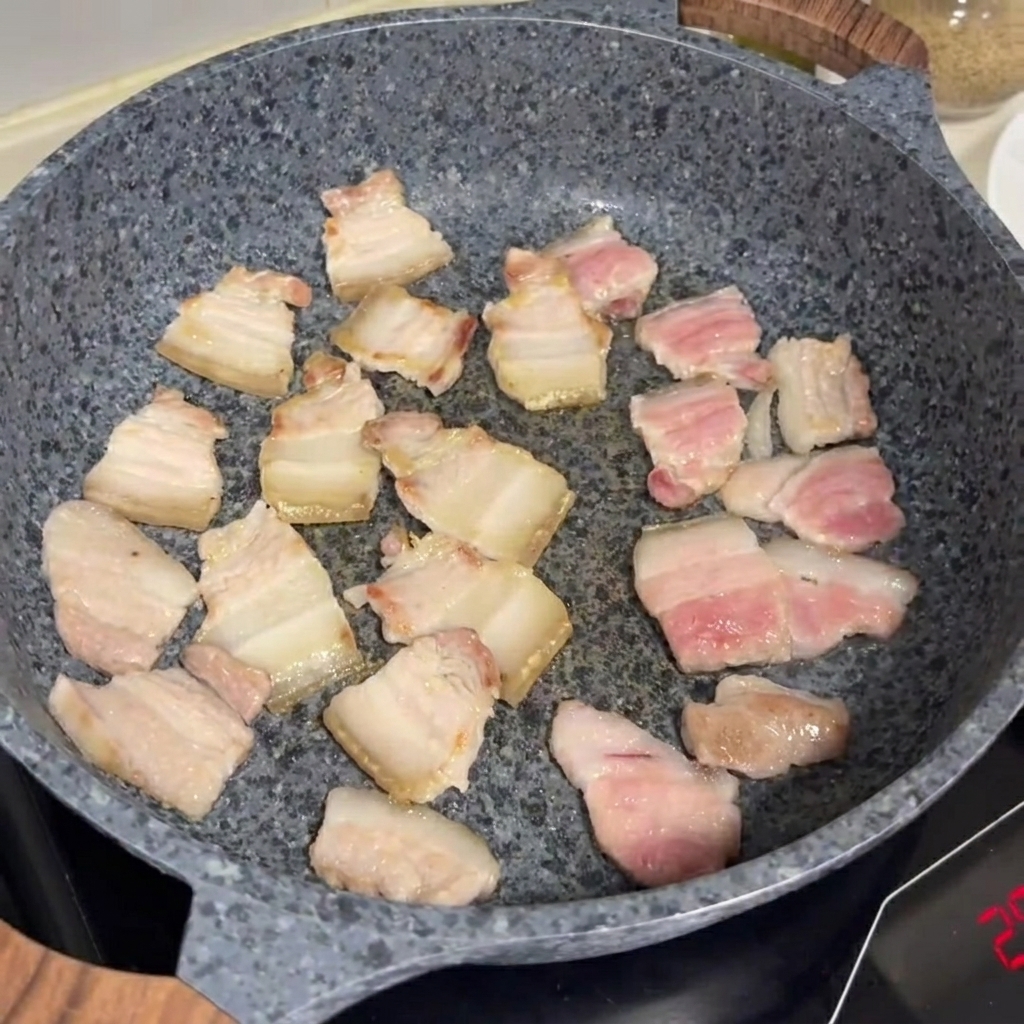 Tranches de poitrine de porc en train de frire et de dorer dans une poêle en pierre grise.