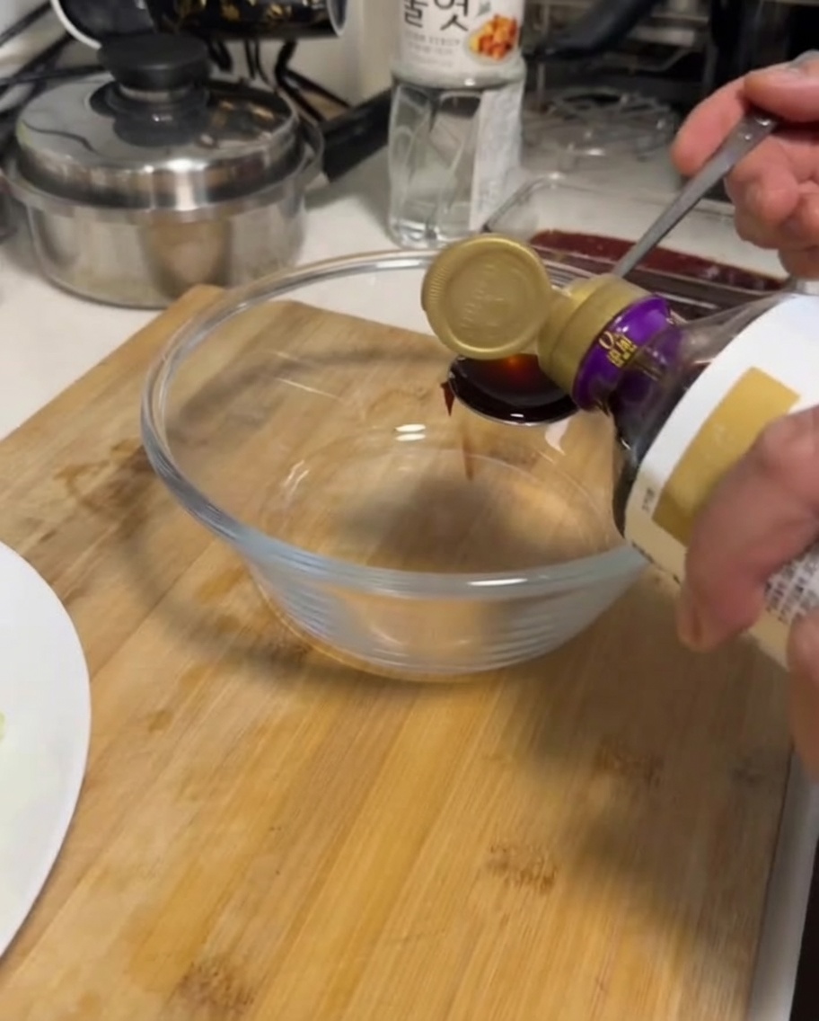 Une main versant de la sauce soja dune bouteille dans un bol en verre transparent.