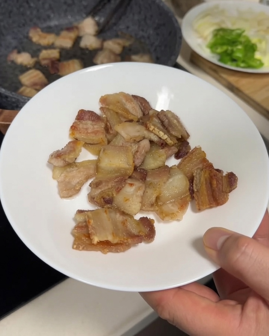 Morceaux de poitrine de porc dorés et croustillants transférés dune poêle vers une assiette blanche avec des pinces en métal.
