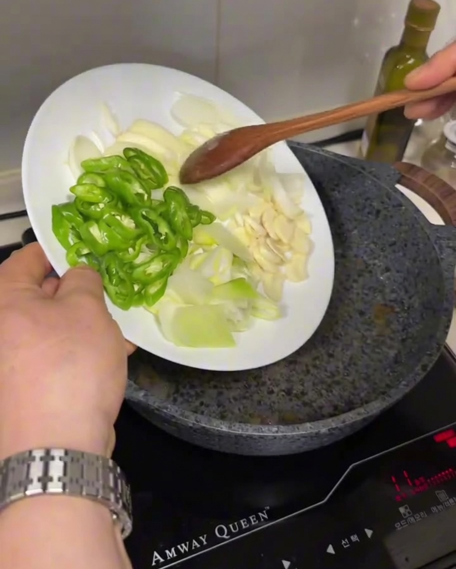 Piments verts tranchés, oignons blancs et ail ajoutés depuis une assiette dans une poêle chaude et huilée.