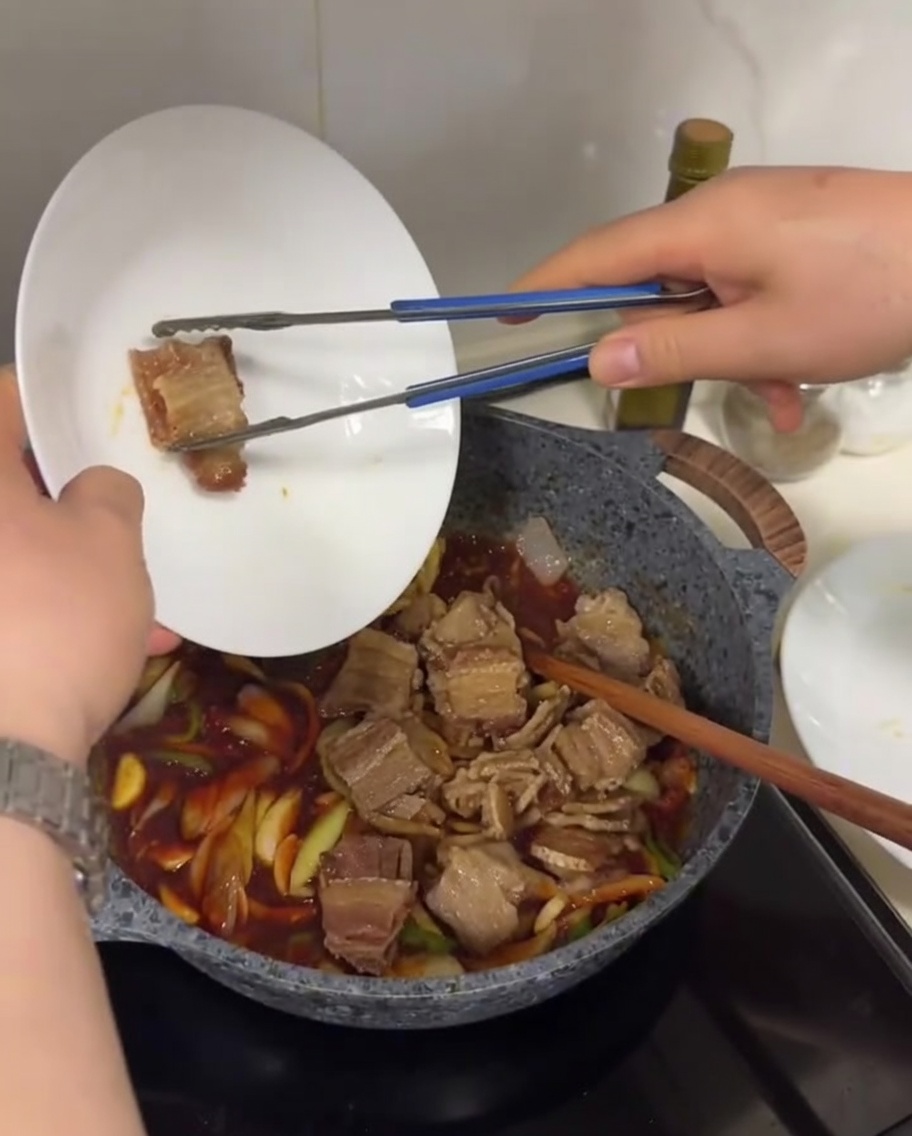 Tranches de poitrine de porc croustillantes ajoutées dans une poêle avec des oignons, poivrons et une riche sauce au piment rouge bouillonnante.