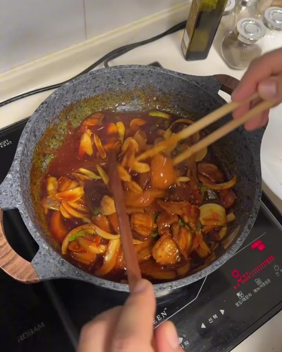 Mélange de poitrine de porc et de légumes sauté dans une sauce rouge sombre et brillante avec de longues baguettes en bois dans une poêle antiadhésive.