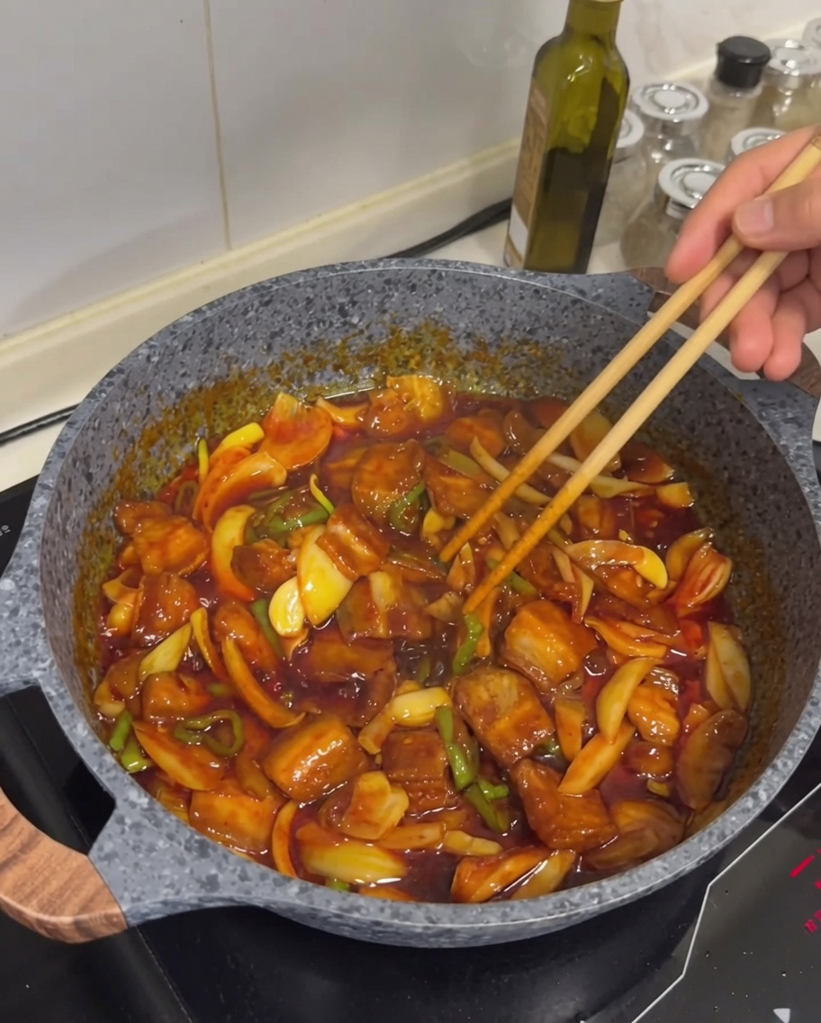 Le plat fini de poitrine de porc sautée épicée avec de la viande dorée, une sauce brillante et une légère dispersion de graines de sésame blanc sur le dessus.