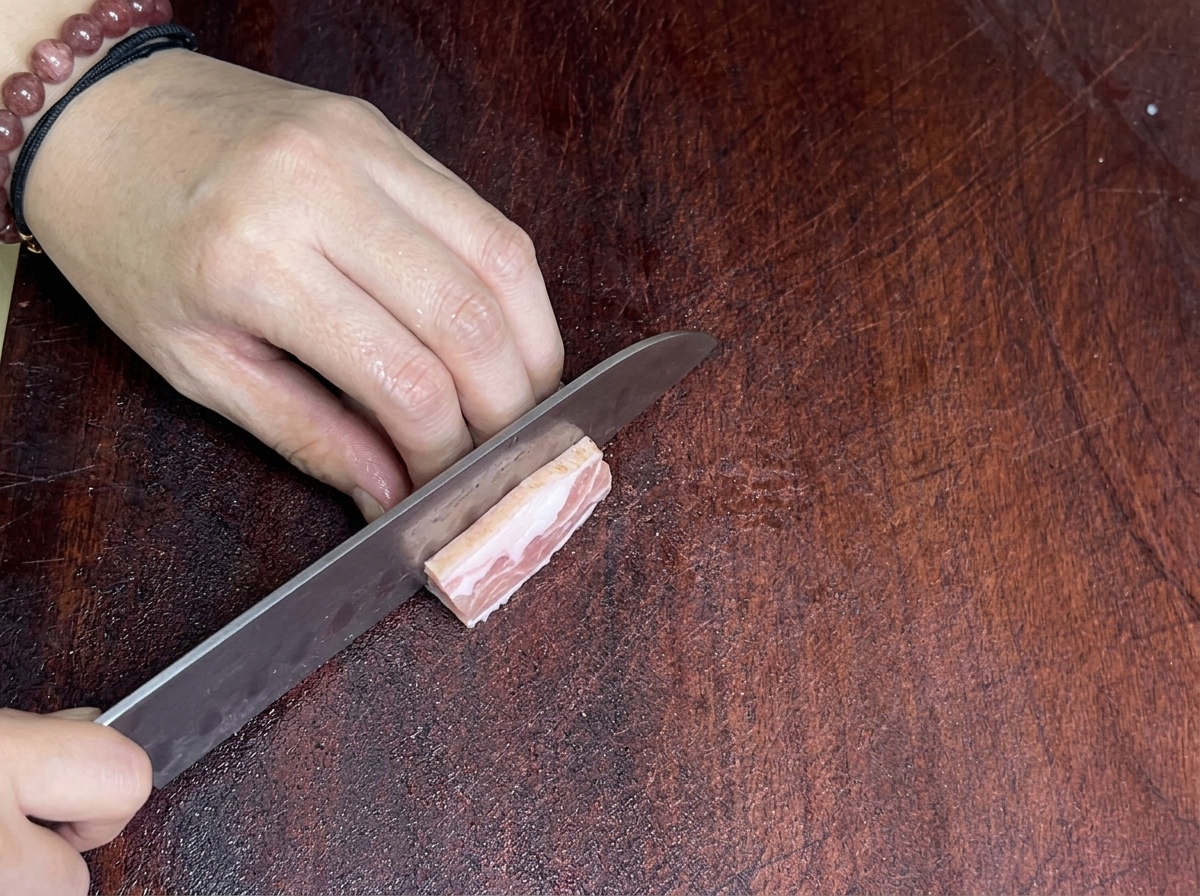 Gros plan dun couteau bien aiguisé tranchant un morceau de poitrine de porc sur une planche à découper en bois.