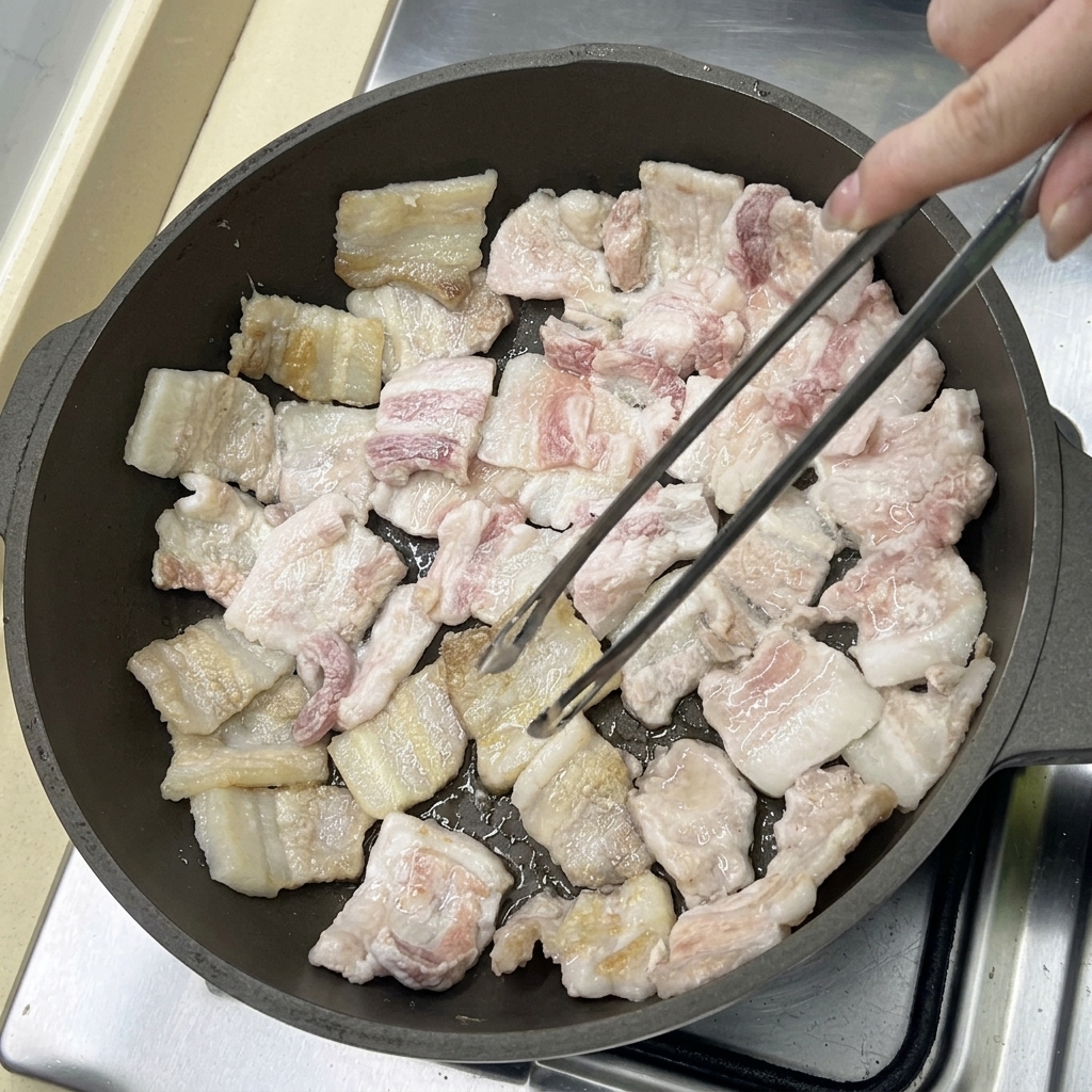 Tranches de poitrine de porc en train de frire dans une poêle, devenant dorées à mesure que le gras fond.