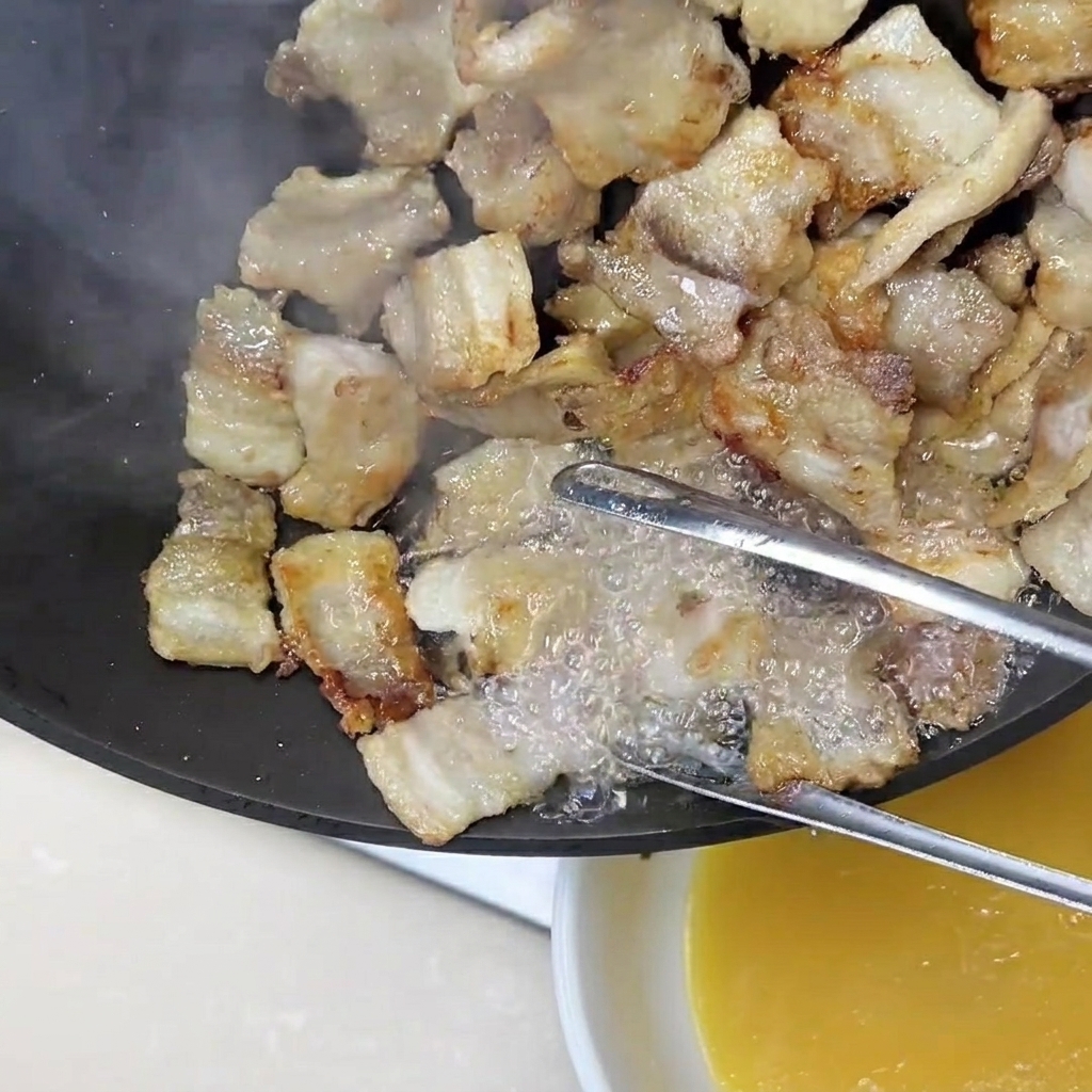 Une pince tenant des tranches de poitrine de porc pendant que lexcès de gras doré est versé hors de la poêle.