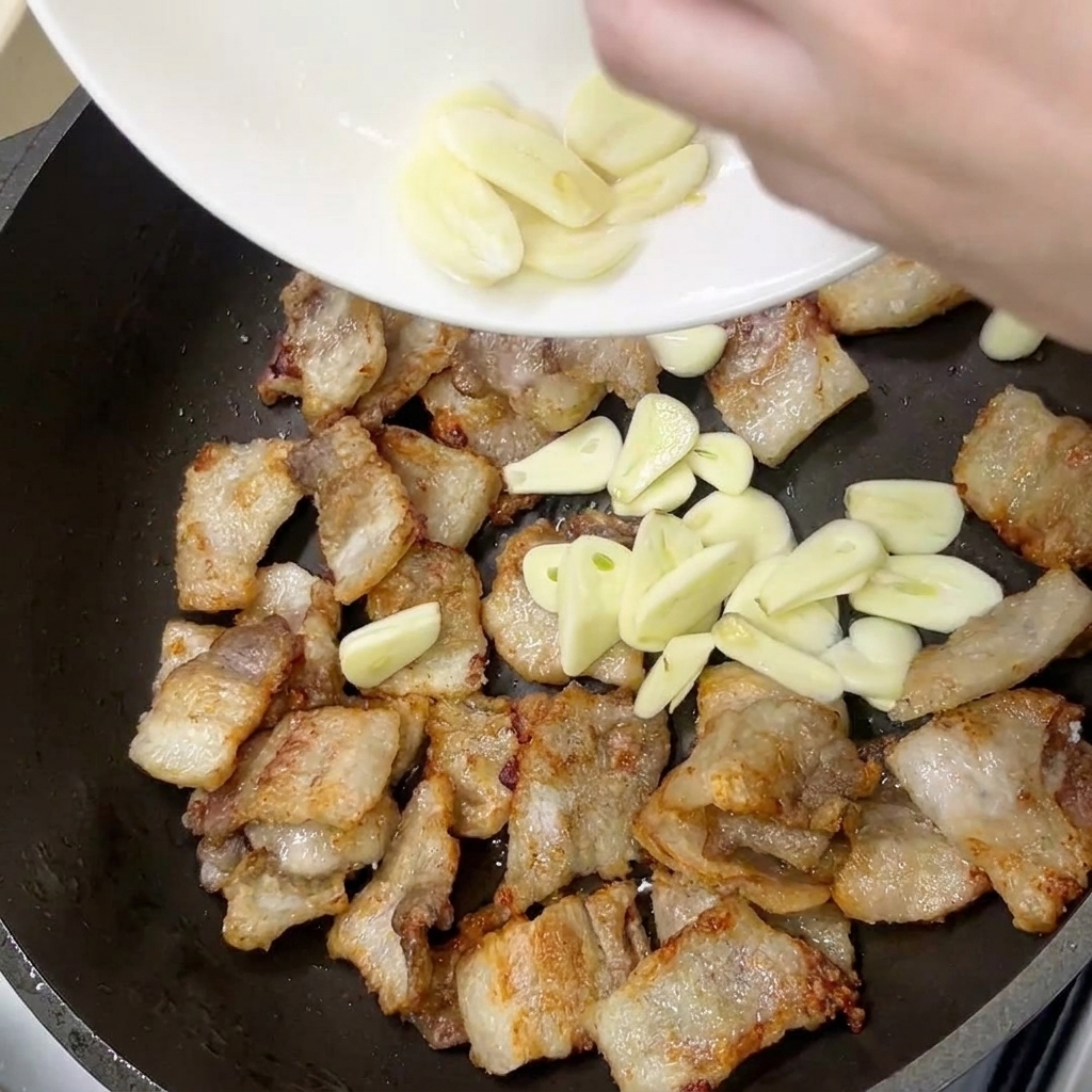 Tranches dail frais ajoutées dans la poêle avec la poitrine de porc dorée.