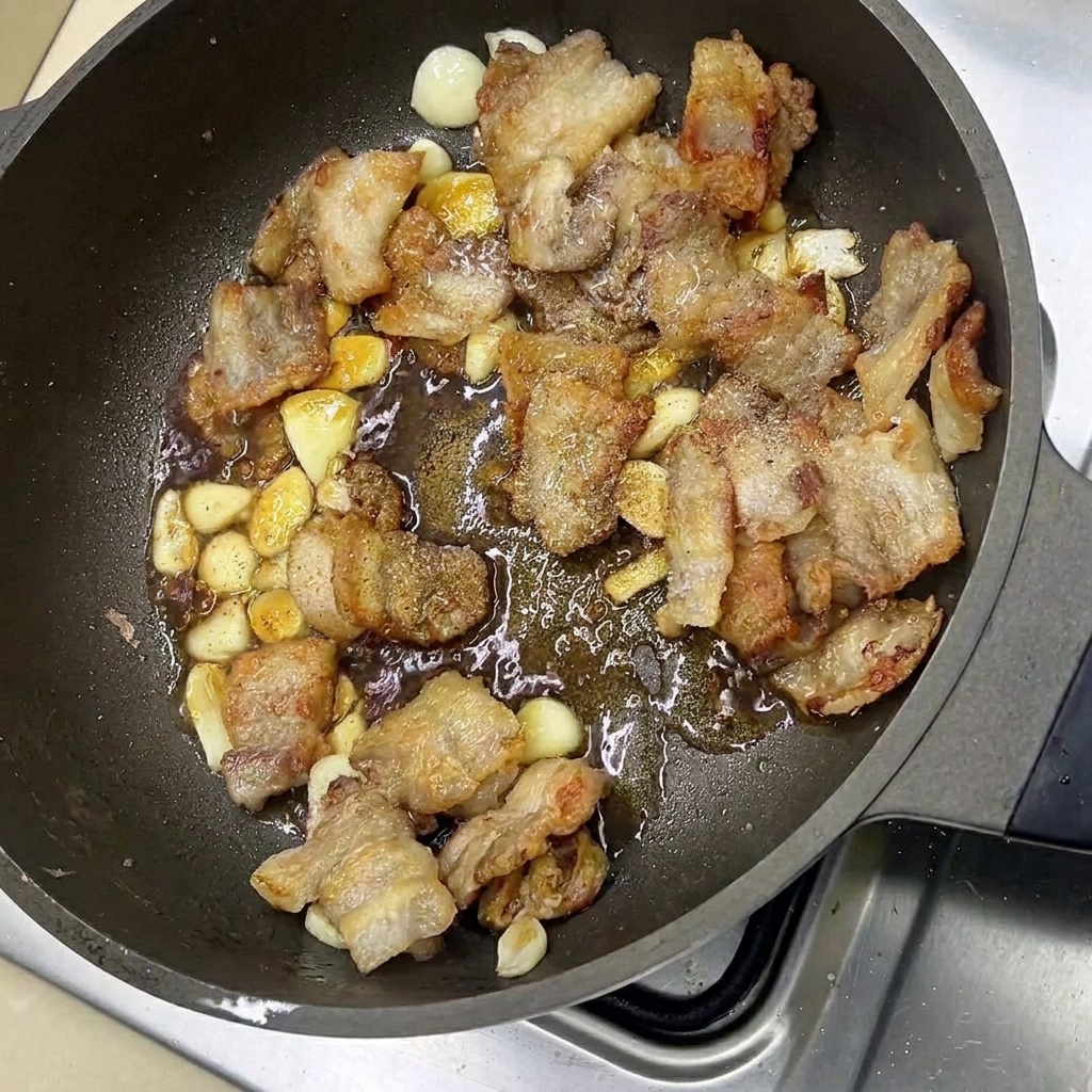 Tranches de poitrine de porc glacées et gousses dail remuées dans une poêle avec les assaisonnements.