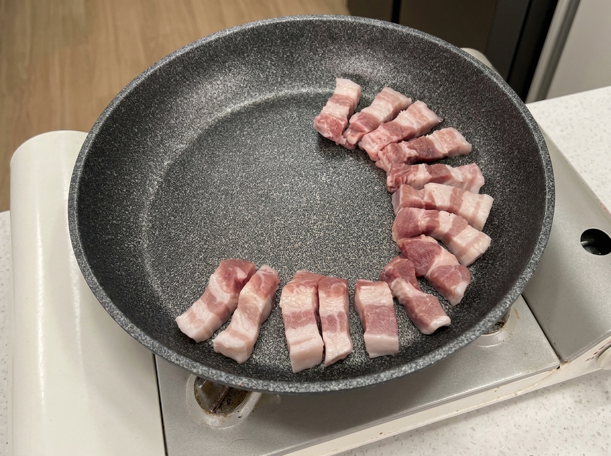 Tranches de poitrine de porc crue disposées en cercle dans une poêle antiadhésive grise.
