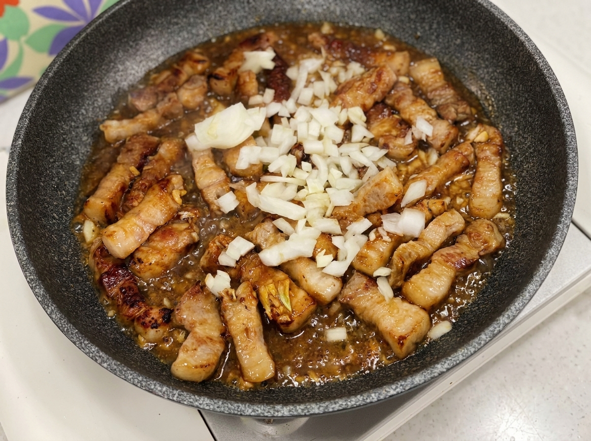 Oignons blancs hachés ajoutés dans une poêle avec le porc et la sauce bouillonnante.