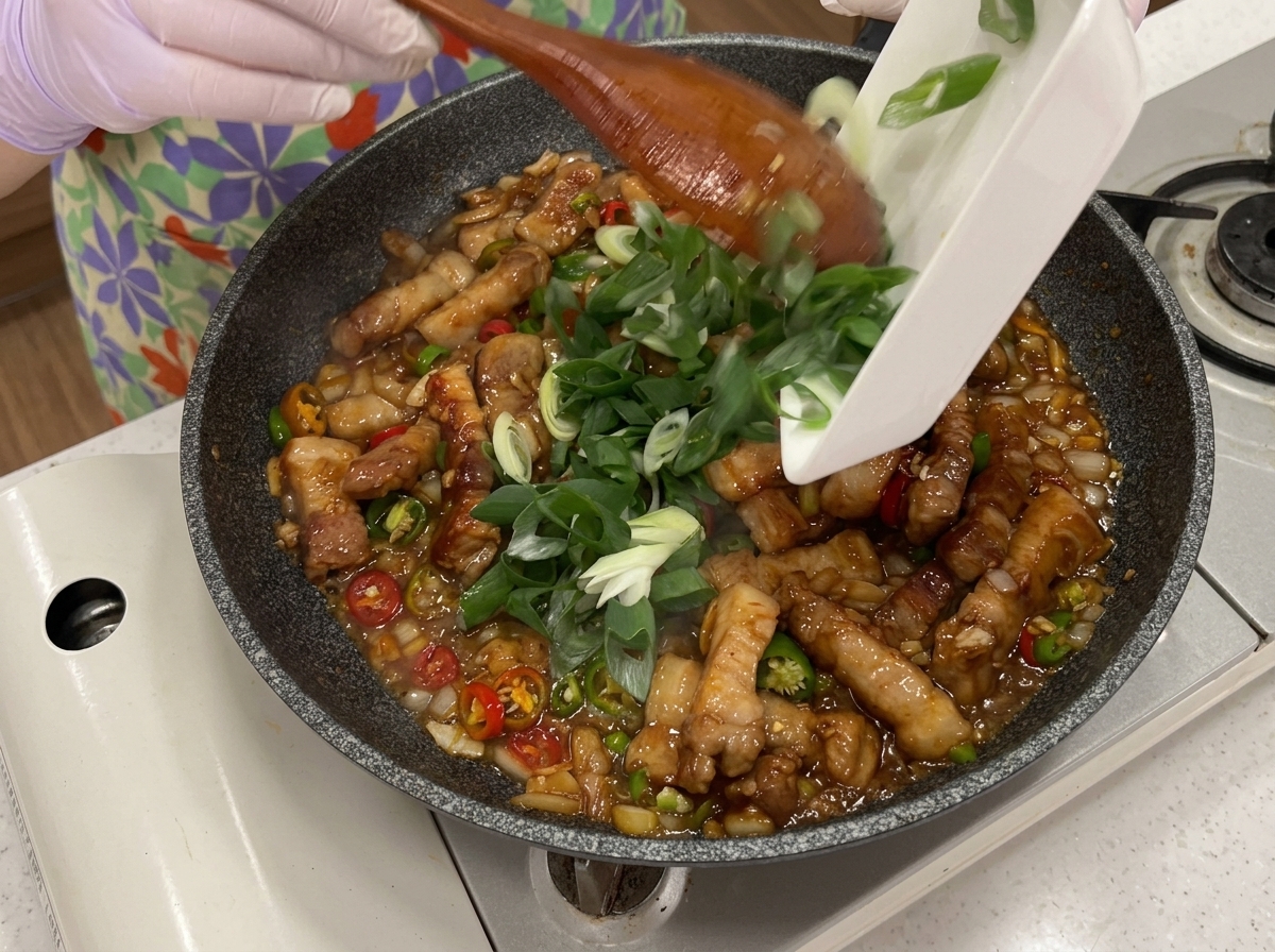 Piments verts, rouges et cébettes ajoutés dans la poêle de porc sauté.