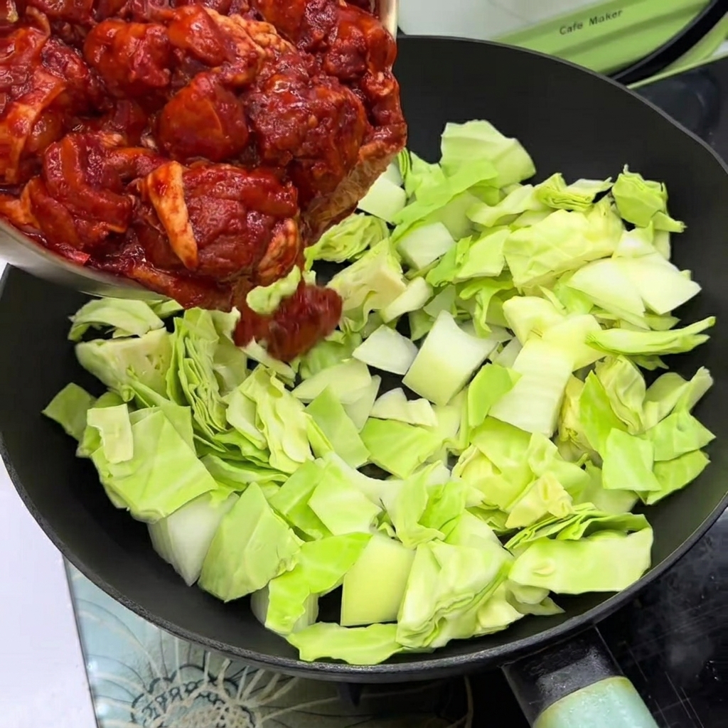 Morceaux de poulet mariné déposés sur le chou et les oignons dans une poêle.
