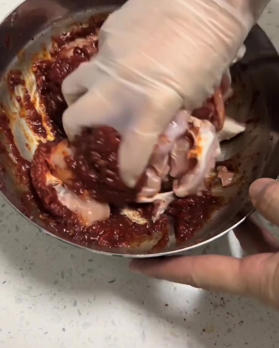 Des morceaux de poulet crus massés à la main dans une marinade rouge.