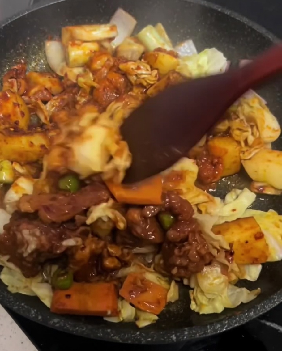 Une spatule mélangeant délicatement le poulet et les légumes dans une poêle chaude.