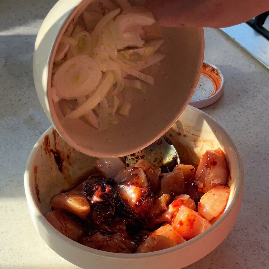 Oignons tranchés et ail haché ajoutés dans un bol de poulet mariné.