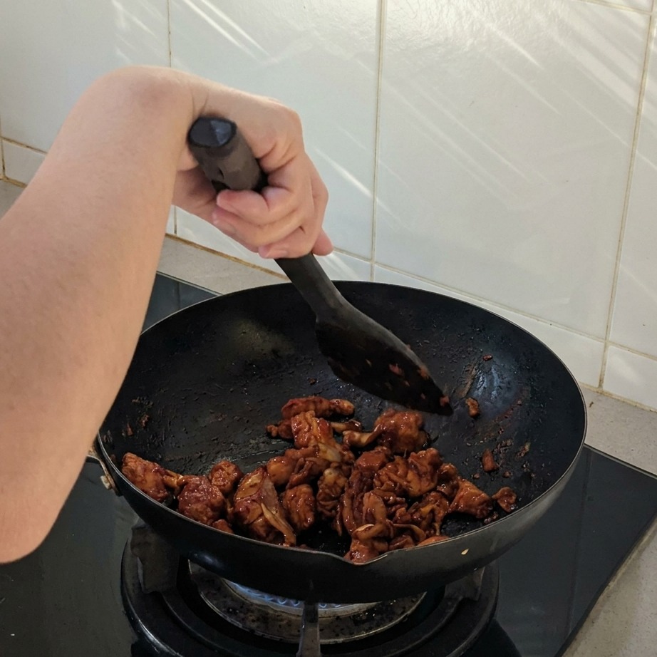 Morceaux de poulet et doignons sautés dans un wok noir, enrobés dune sauce épicée.