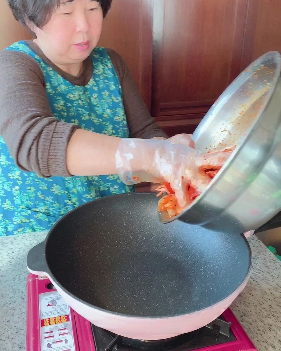 Le mélange de poitrine de porc et de calamar marinés est versé dun bol en inox dans une poêle chaude.