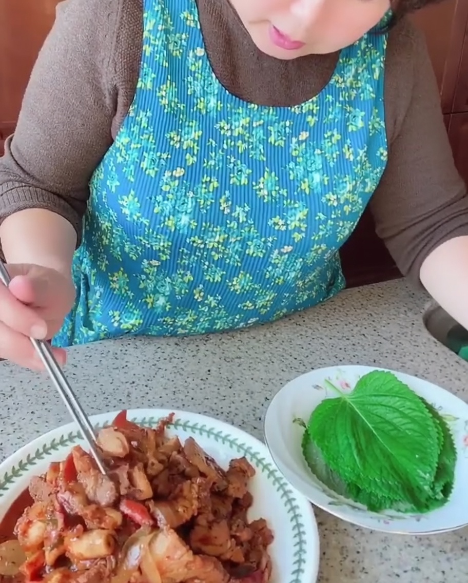 Une personne utilisant des baguettes pour placer un morceau de poitrine de porc cuite et de calamar sur une feuille de perilla verte bien fraîche.