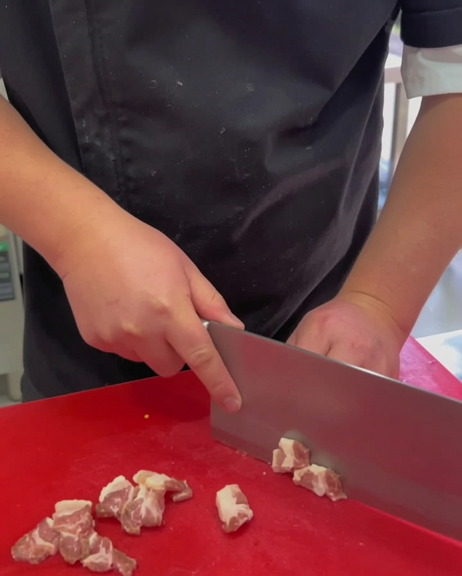 De fines tranches de poitrine de porc crue disposées sur une planche à découper rouge.