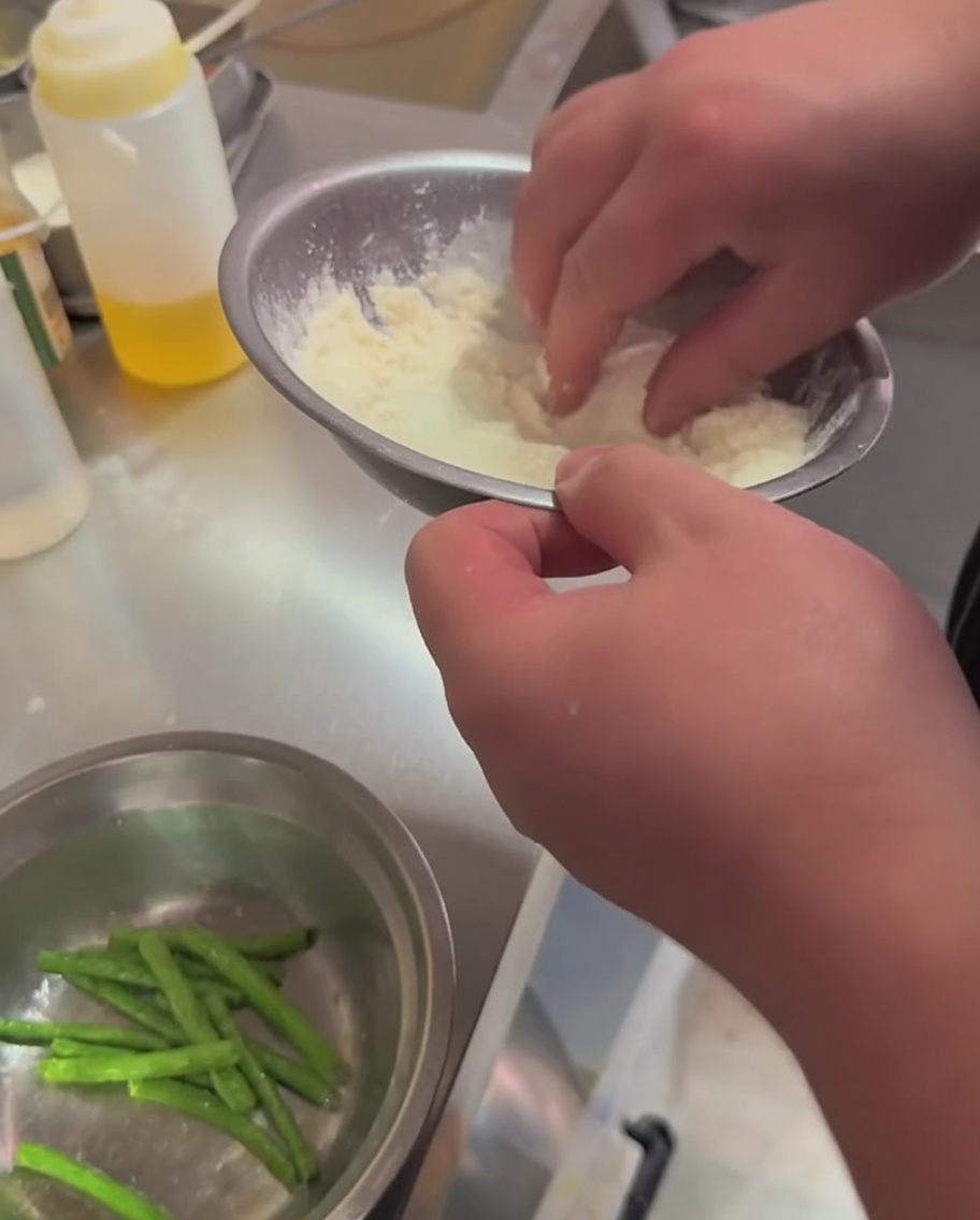 Des haricots verts mélangés avec de la farine et des épices dans un cul-de-poule en métal.