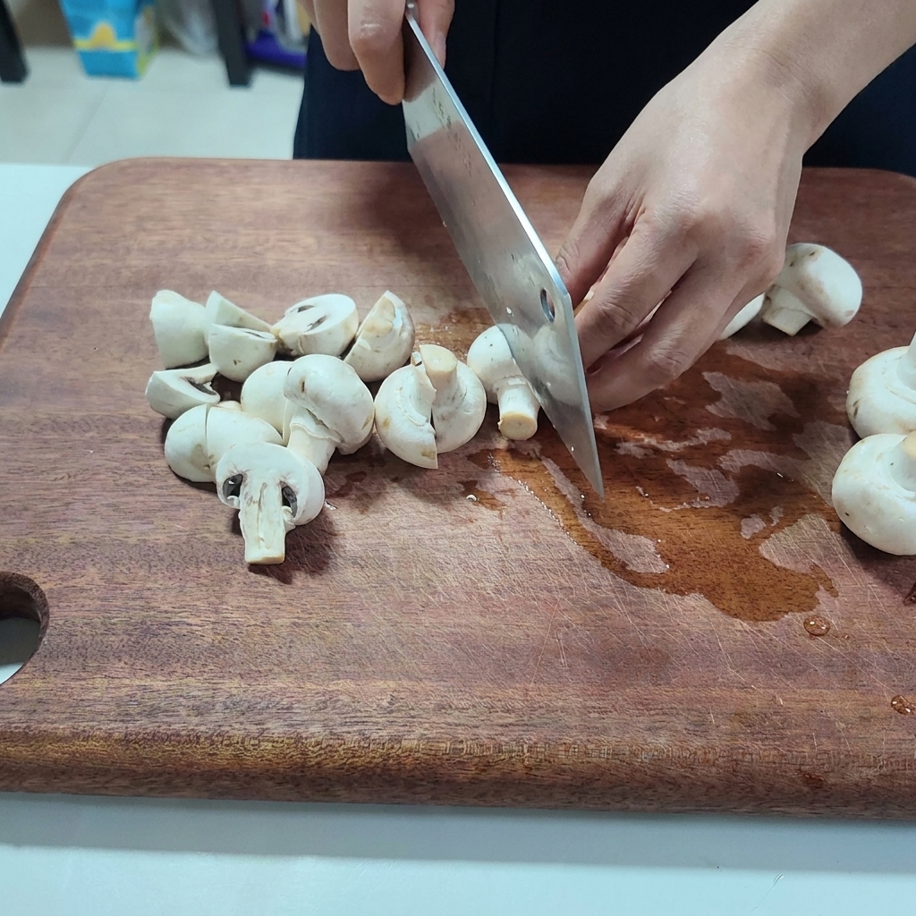 Champignons de Paris frais coupés en deux sur une planche à découper en bois.