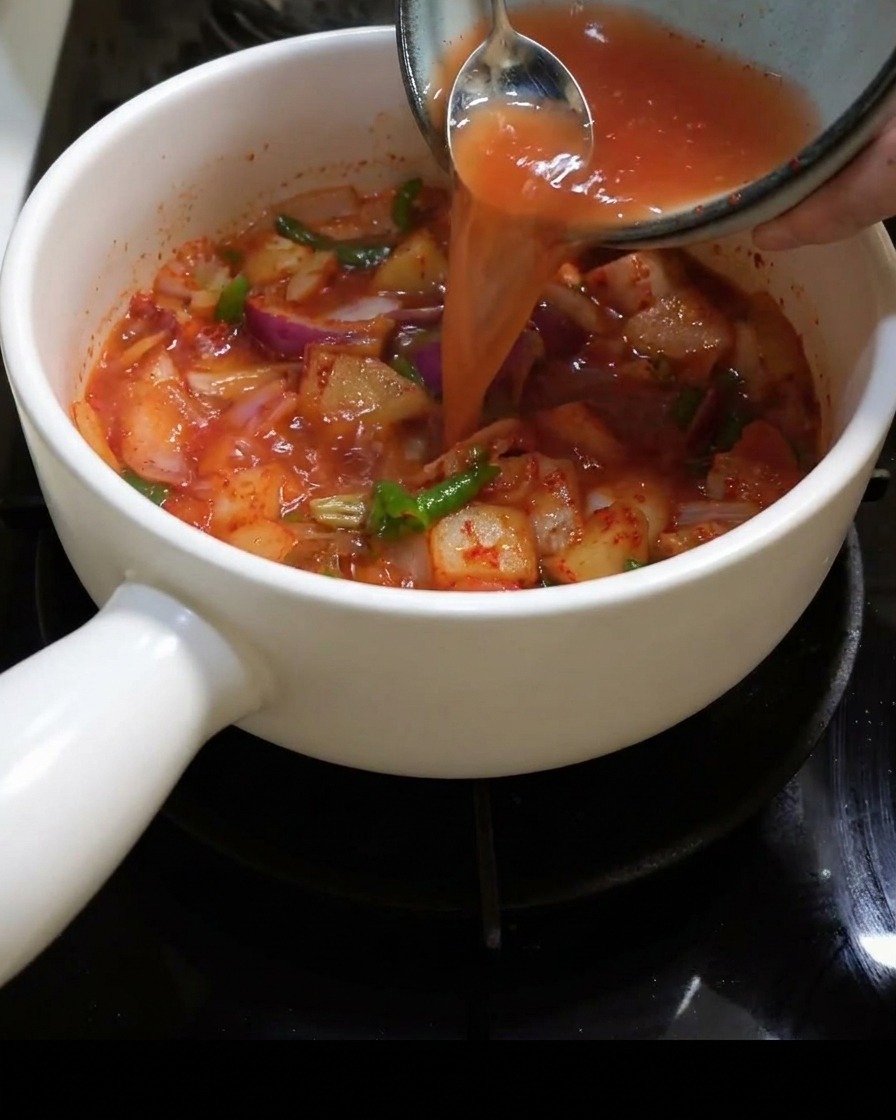De leau est versée dans la marmite remplie de kimchi et doignons.