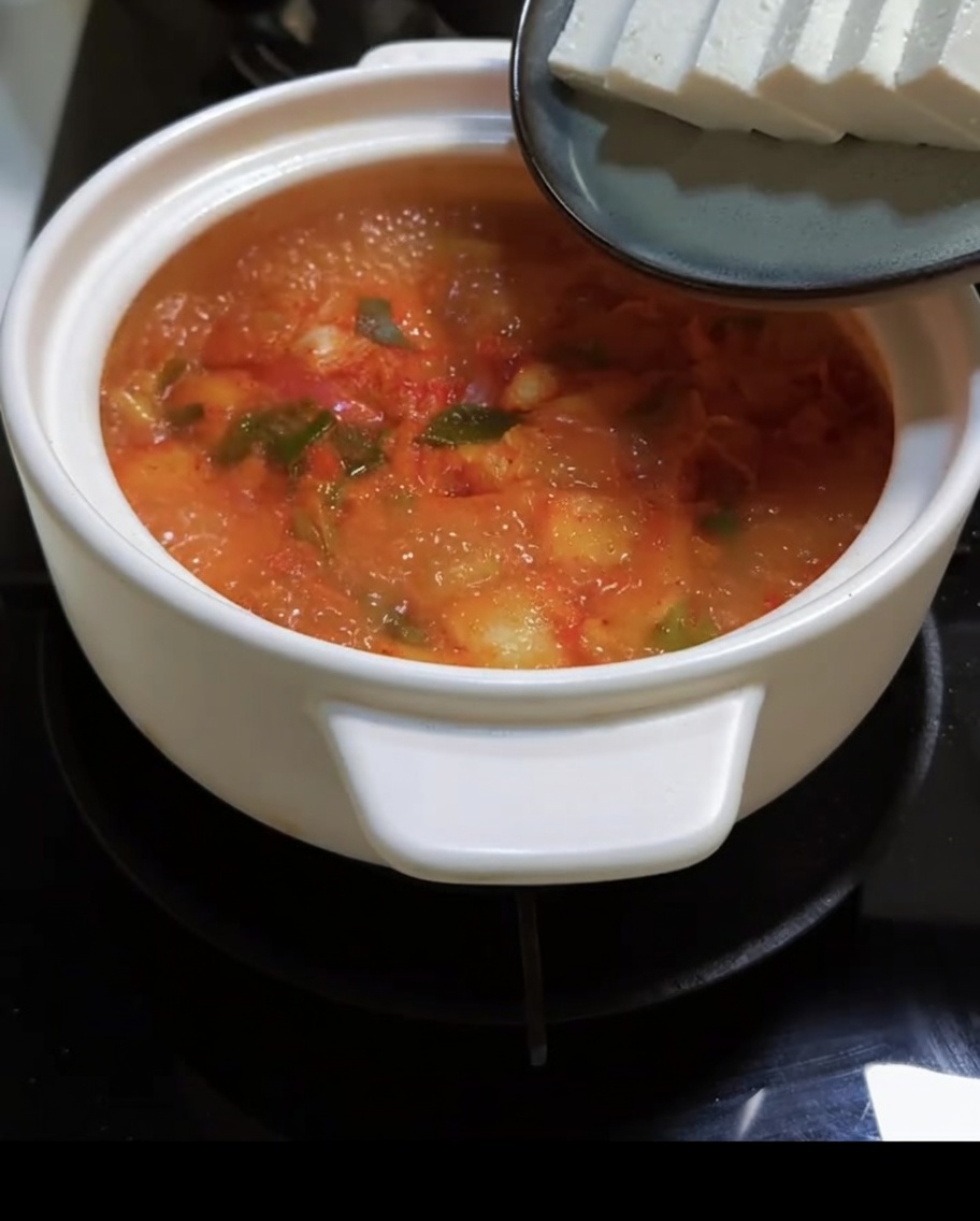Des morceaux de tofu sont délicatement déposés dans la soupe rouge bouillonnante.
