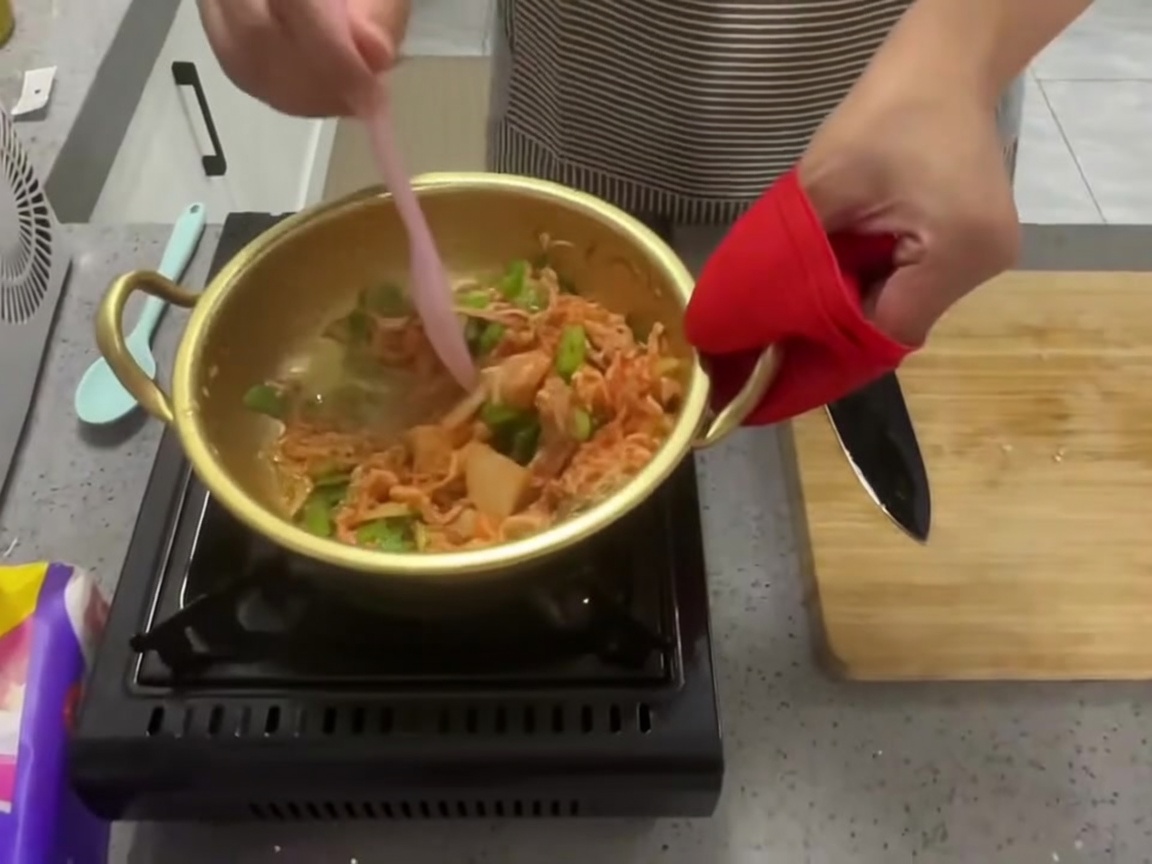 Kimchi, oignons verts et ail mélangés dans la marmite avec une spatule en silicone rose.