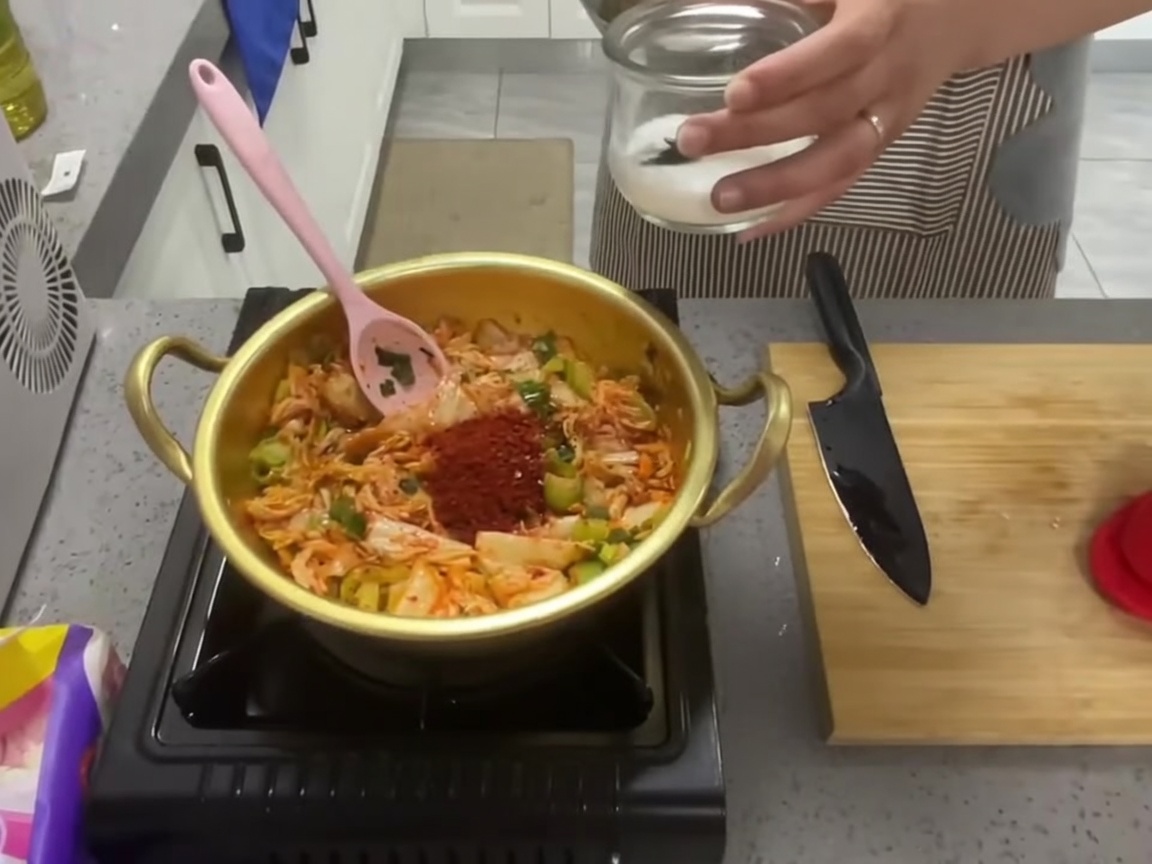 Une cuillerée de sucre blanc ajoutée au mélange de kimchi assaisonné dans la marmite.