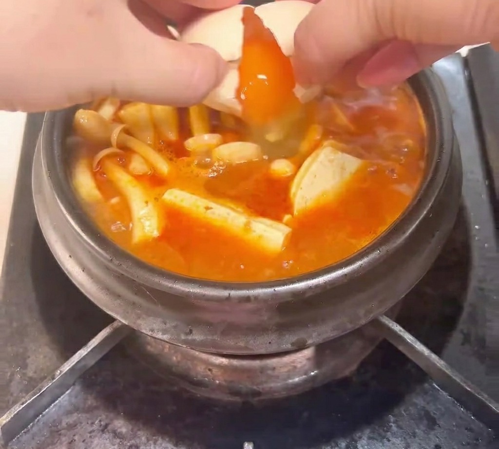 Un œuf cru cassé dans le caquelon bouillonnant rempli de kimchi, thon, champignons et tofu.