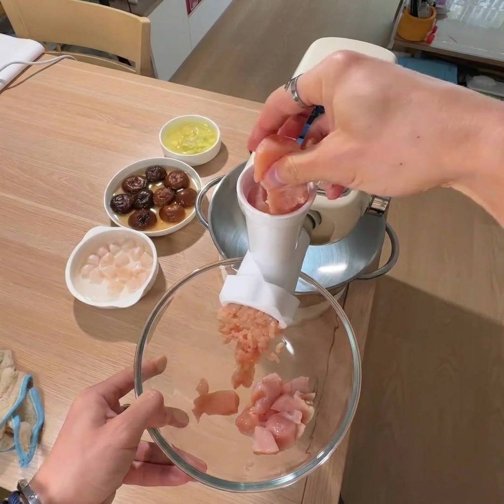 Une main plaçant des morceaux de blanc de poulet dans un grand bol avec des bols de champignons et pétoncles en arrière-plan.